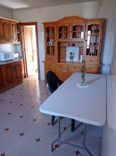 Cocina luminosa con muebles de madera, mesa blanca y una planta decorativa en el centro.