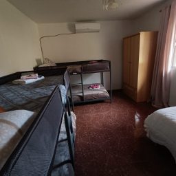 Dormitorio con literas y una cama individual, armario y ventana con cortinas.