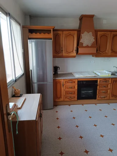 Cocina con muebles de madera, nevera plateada, horno y suelo con detalles en blanco y naranja.