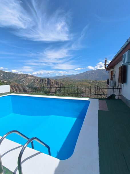 Vista de una piscina azul rodeada de montañas y cielo despejado.