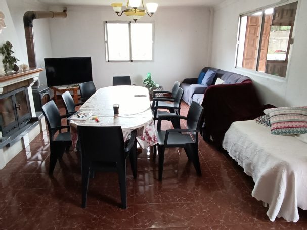 Sala de estar con mesa, sillas, sofá y televisor en un ambiente luminoso.