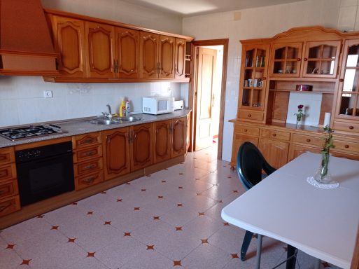 Cocina con muebles de madera, mesa blanca y detalles decorativos en la pared.