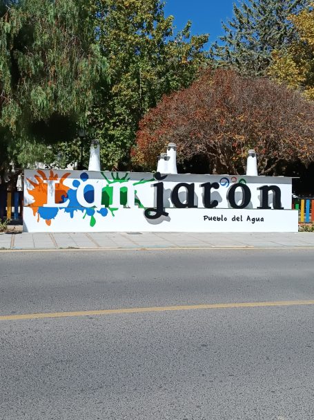 Letrero colorido que dice "Jardín" con arte urbano y fondo de árboles.