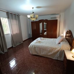 Habitación amplia con cama doble, armario de madera y luz suave. Cortinas grises.