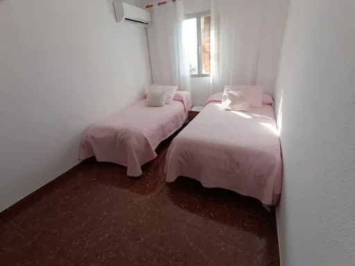 Habitación con dos camas individuales, paredes blancas y luz natural.