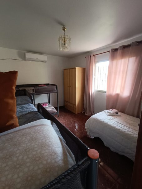 Habitación con dos camas, armario y ventana con cortinas. Ambiente iluminado y acogedor.