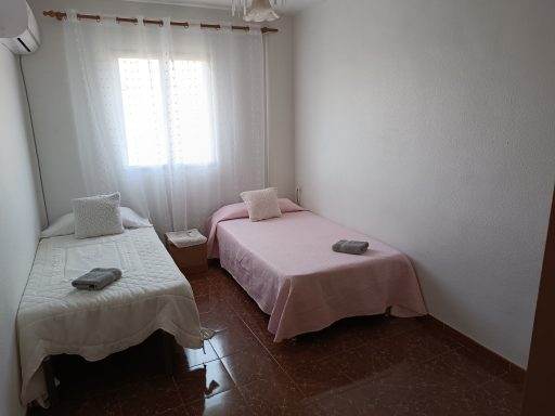 Habitación con dos camas, una con sábanas rosas y otra con sábanas blancas, luz natural.