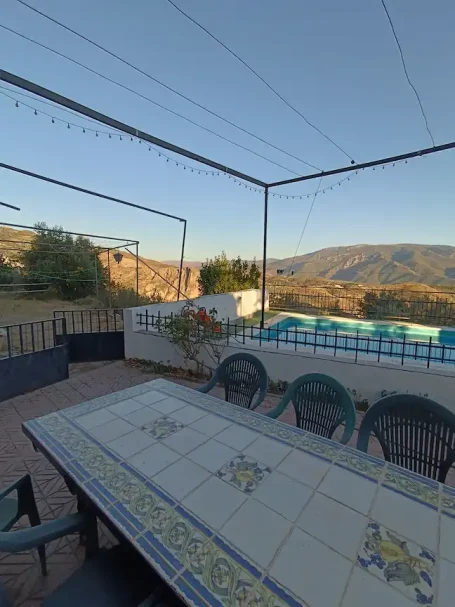 Terraza con mesa y sillas, rodeada de vegetación y vistas a montañas.