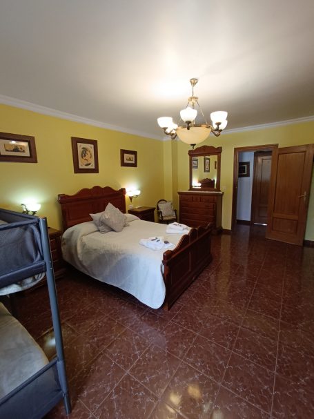 Habitación con cama doble, litera, muebles de madera y paredes amarillas.
