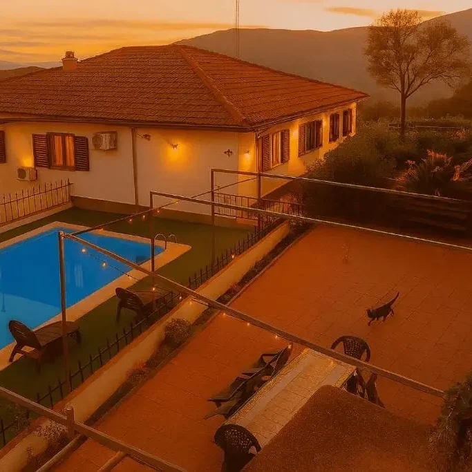 Casa con piscina al atardecer, rodeada de naturaleza y sillas en el patio.