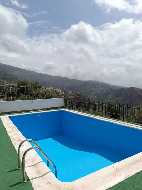Piscina vacía de color azul rodeada de paisaje montañoso y cielo nublado.