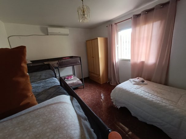 Habitación con dos camas, armario de madera y ventana con cortinas rosadas.