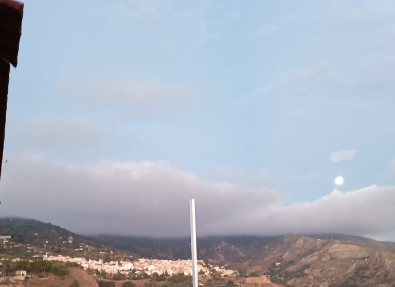 Paisaje montañoso con niebla y un cielo parcialmente nublado, luna visible. Vistas del Cortijo