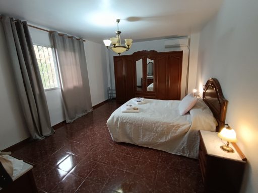 Habitación amplia con cama, cortinas grises y muebles de madera. Suelo de cerámico brillante.