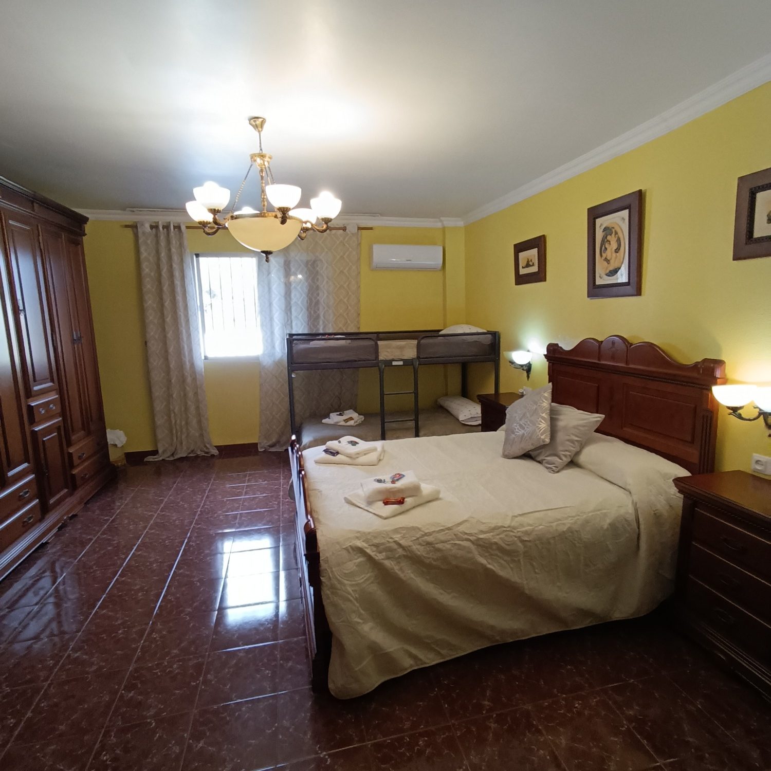 Habitación luminosa con cama doble, cuna, armario y decoración en tonos amarillos.