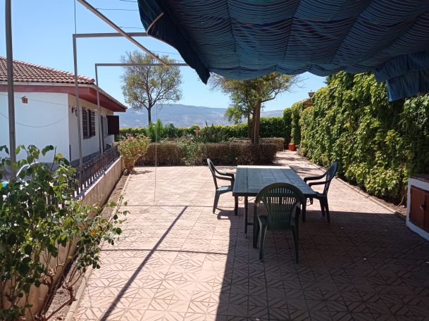 Terraza con mesa y sillas, rodeada de vegetación y vistas a montañas.