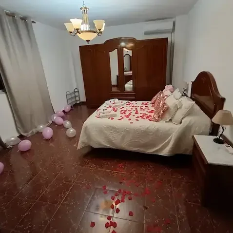 Habitación decorada con pétalos de rosa, globos y una cama con sábanas claras.