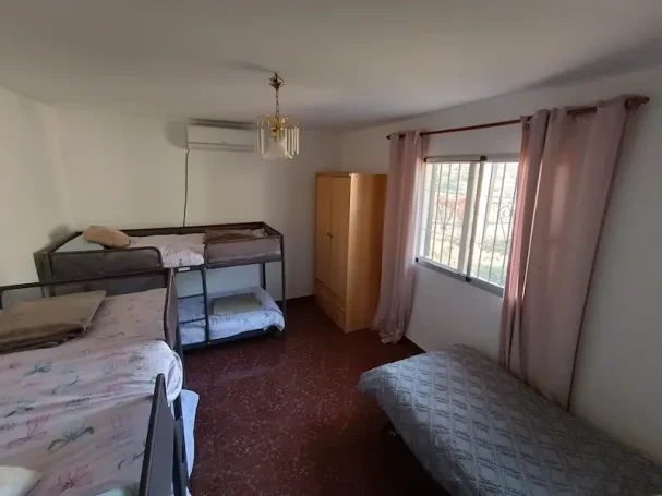 Habitación simple con literas, una cama individual y luz natural que entra por la ventana.