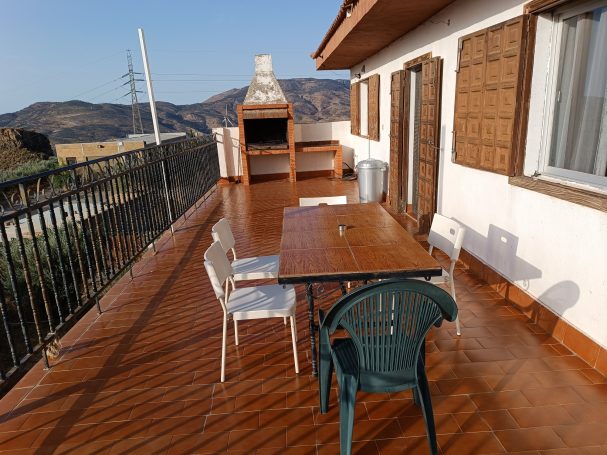 Terraza con mesa, sillas y barbacoa, rodeada de montañas y con buena iluminación.