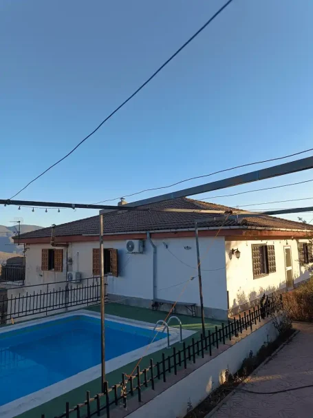 Casa con piscina al aire libre, cielo despejado y vista de montañas al fondo.