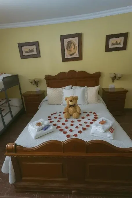 Cama decorada con pétalos de rosa y un oso de peluche en el centro.
