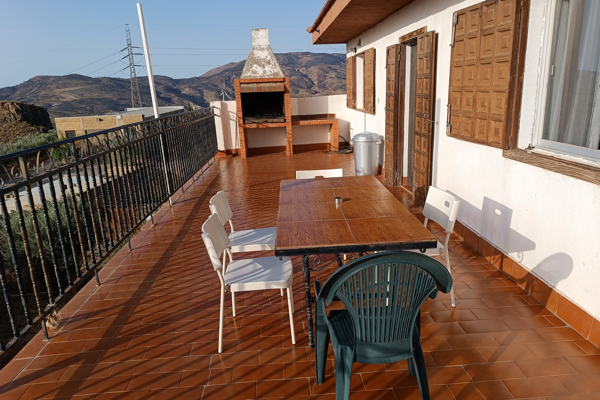Mesa con sillas en una terraza, con vistas a montañas y una barbacoa al fondo.