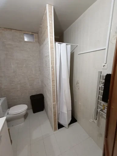 Baño con espejo, lavabo y estantería en una pared. Luz del techo encendida.