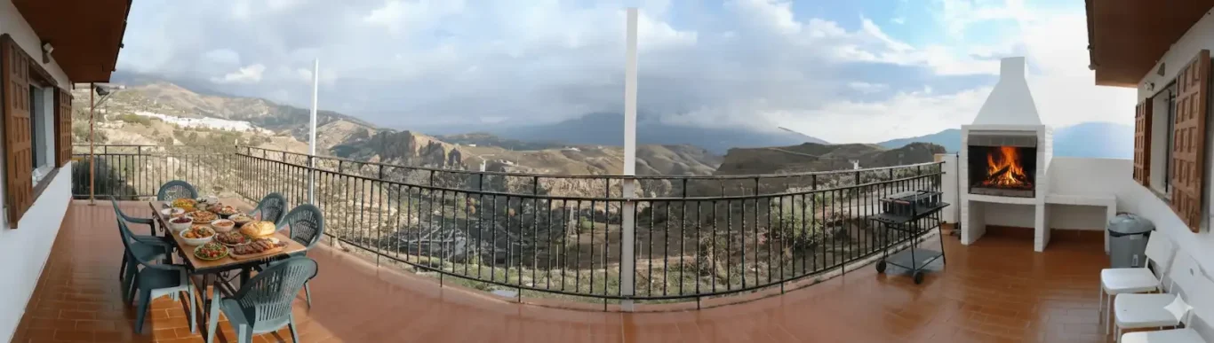 Imagen panorámica de la terraza del Chalet Venta Del Aire con barbacoa de obra blanca encendida, mesa con banquete y vistas despejadas a la 