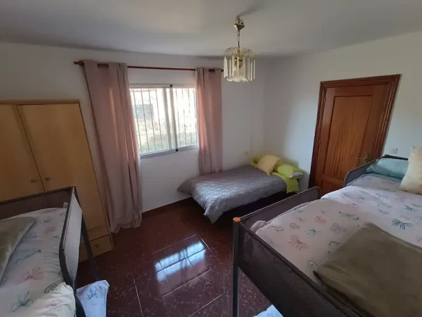 Habitación simple con literas, una cama individual y luz natural que entra por la ventana.