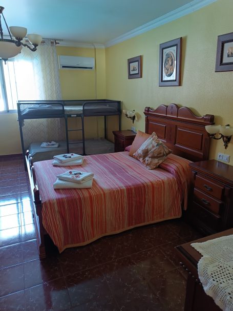 Habitación con cama doble, cuna y decoración en tonos cálidos. Ventana con luz.