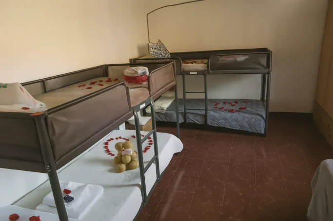 Habitación con tres cunas metálicas y mantas en el suelo.