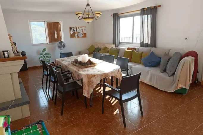 Comedor acogedor con mesa, sillas, sofá y televisión en un ambiente luminoso.