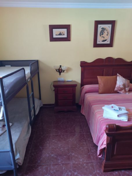 Habitación con cama matrimonial y litera, decorada con cuadros y mesa de noche.