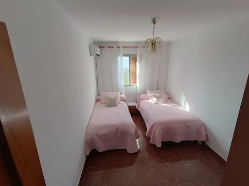 Habitación con dos camas, una con sábanas rosas y otra con sábanas blancas, luz natural.