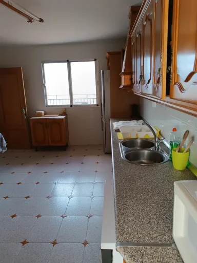 Cocina con muebles de madera, encimera de granito y ventanas iluminadas.
