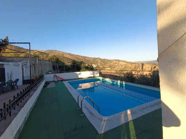 Piscina azul con vista a montañas y cielo con nubes en un día soleado.