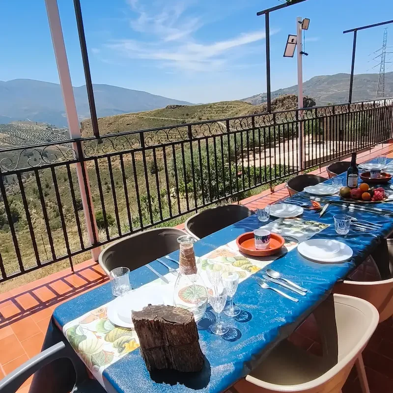 Terraza de Cortijo Terrón con comedor Mesa al aire libre con platos de comida y un oso de peluche en un entorno montañoso.