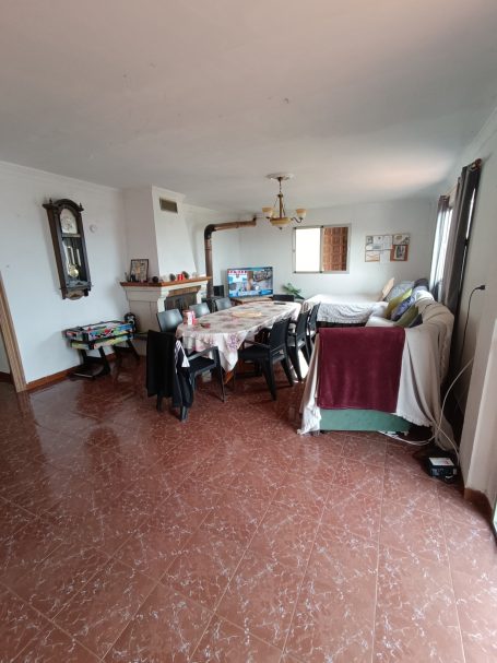 Sala de estar amplia con mesa, sillas y decoración sencilla. Suelo de baldosa brillante.