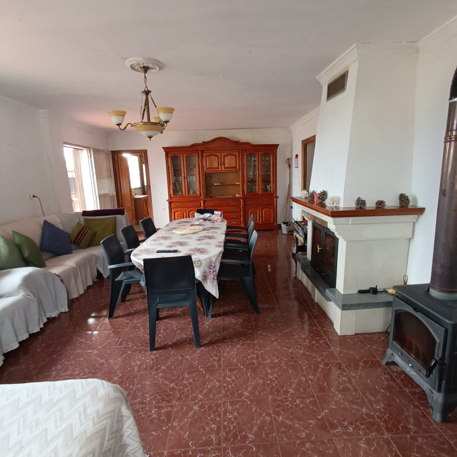 Sala de estar con mesa grande, sillas, sofá y chimenea en un ambiente luminoso.