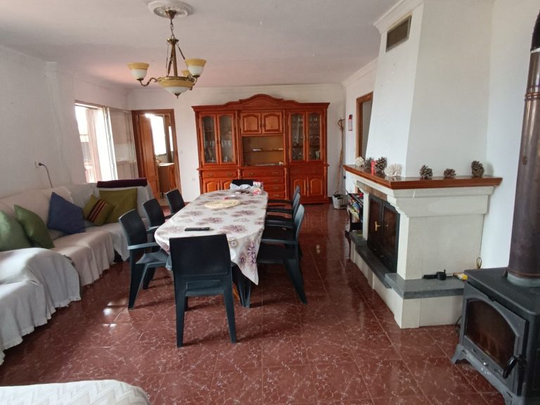 Sala de estar con mesa grande, sillas, sofá y chimenea en una casa.