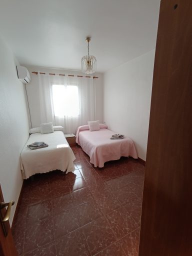 Habitación con dos camas, luces naturales y suelo de azulejos.