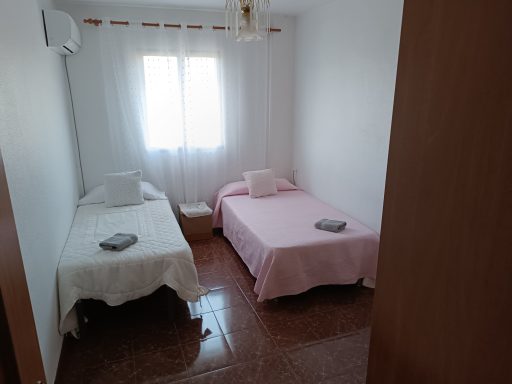 Habitación con dos camas individuales, paredes blancas y luz natural.