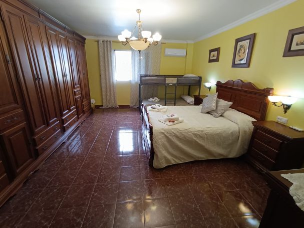 Habitación luminosa con cama grande, muebles de madera y decoración en tonos amarillos.