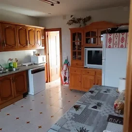 Cocina con muebles de madera, electrodomésticos y mesa en el centro.