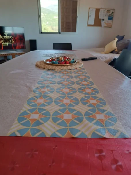 Mesa con mantel decorativo y bandeja de dulces, en un ambiente luminoso.