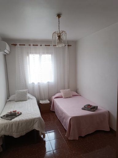 Habitación con dos camas, luz natural y cortinas blancas. Decoración sencilla.
