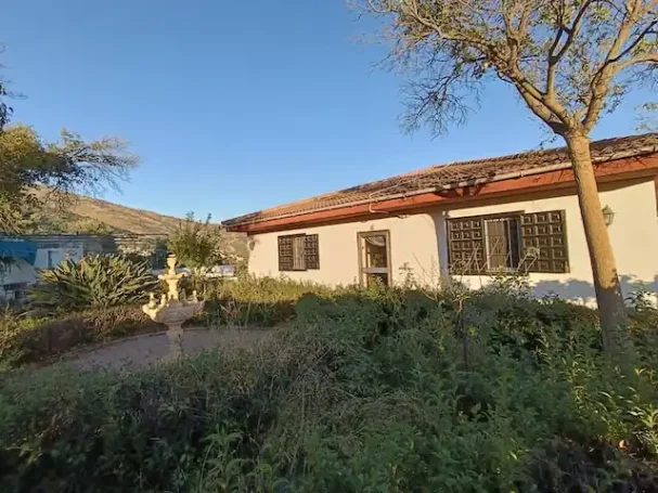 Vista panorámica de un jardín con piscina, casas y montañas al fondo.