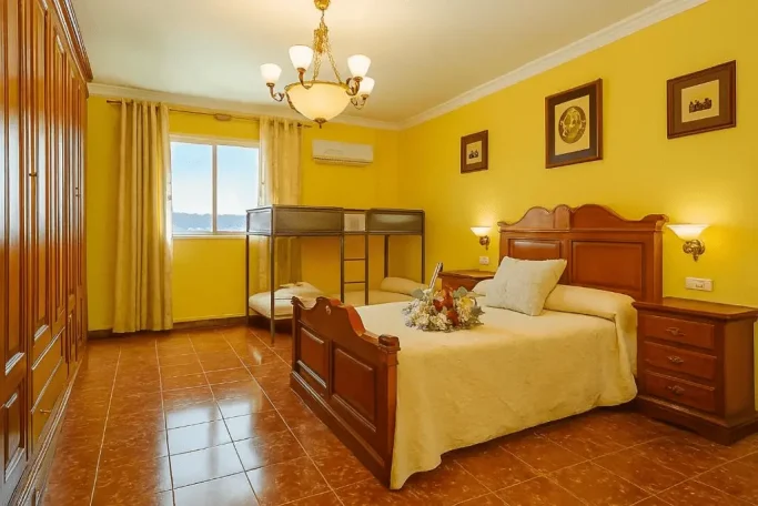 Habitación con cama doble, cuna y decoración en tonos cálidos. Ventana con luz.