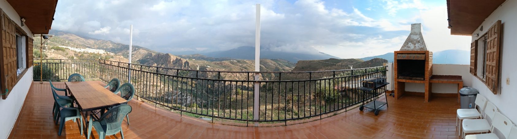 Vista panorámica de un paisaje montañoso con una terraza y muebles exteriores.