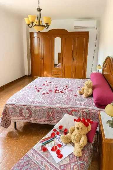 Habitación con cama decorada con pétalos de rosa y ositos de peluche en la cama.